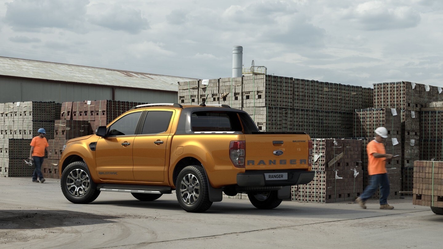 Ford Ranger in Orange. Dreiviertelansicht von hinten, parkend auf einem Bauhof