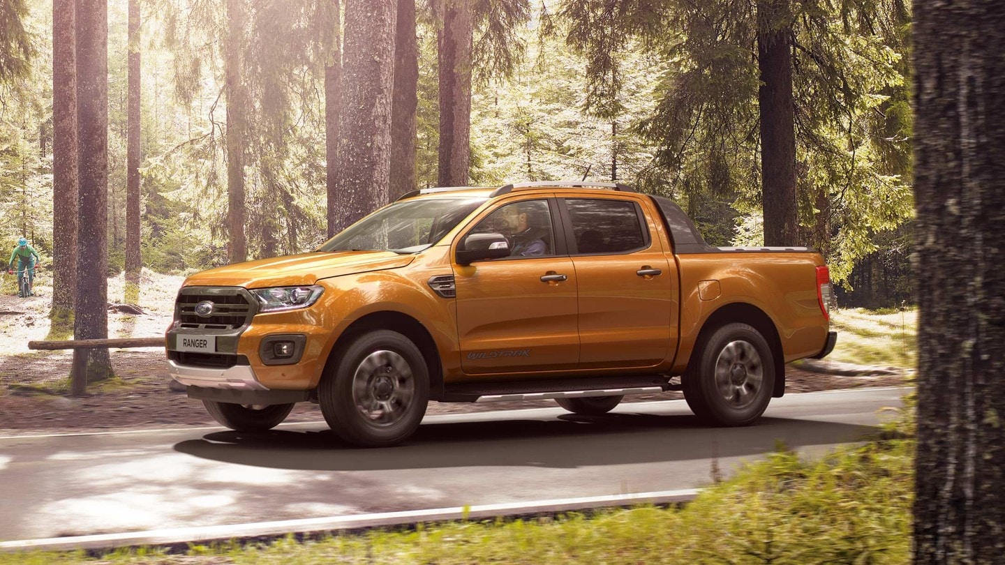 Ford Ranger in Orange. Seitenansicht, fahrend auf einer Forststraße