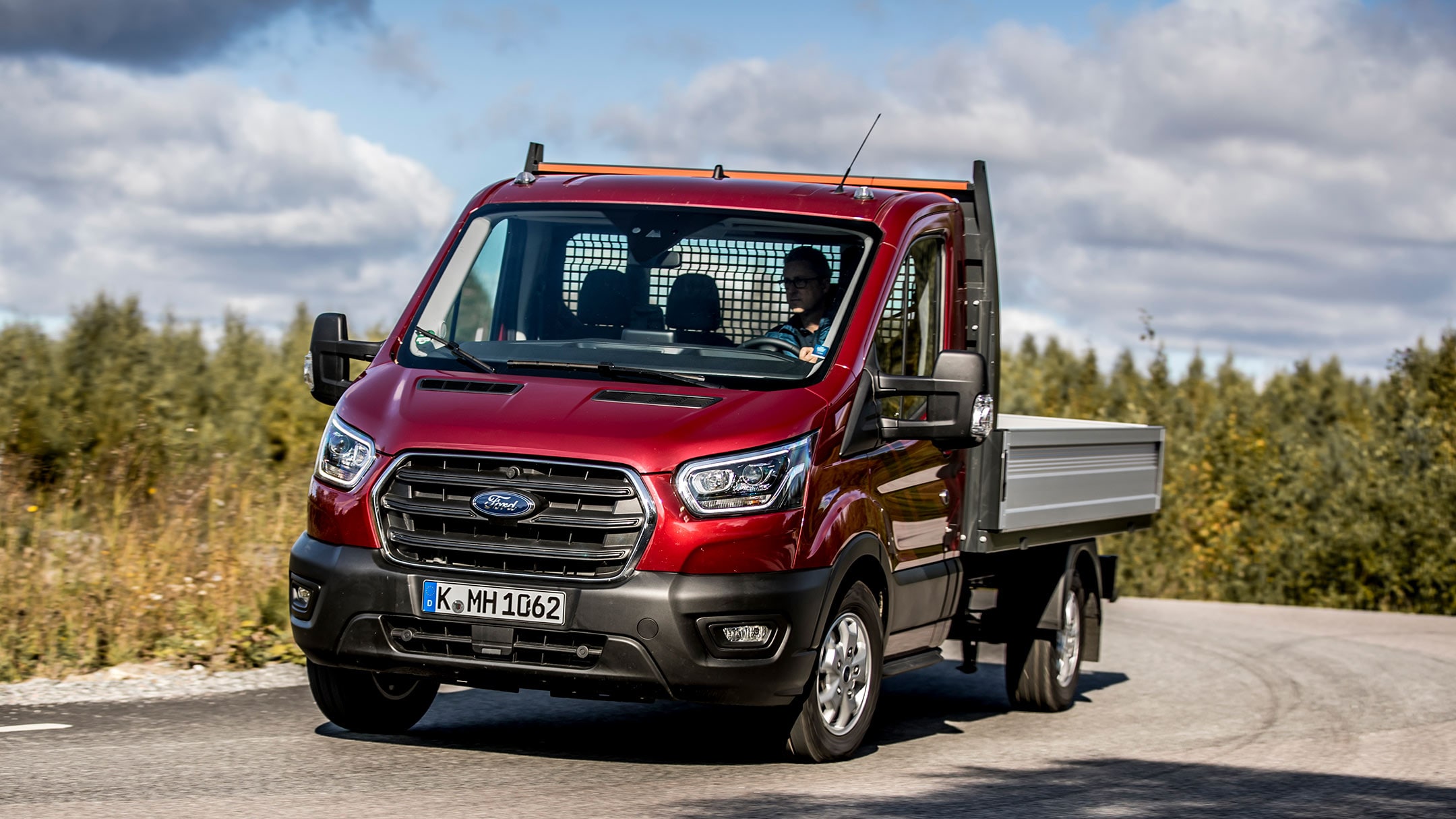 Ford Transit Pritschenwagen in Rot. Dreiviertelansicht, in Bewegung auf Landstraße