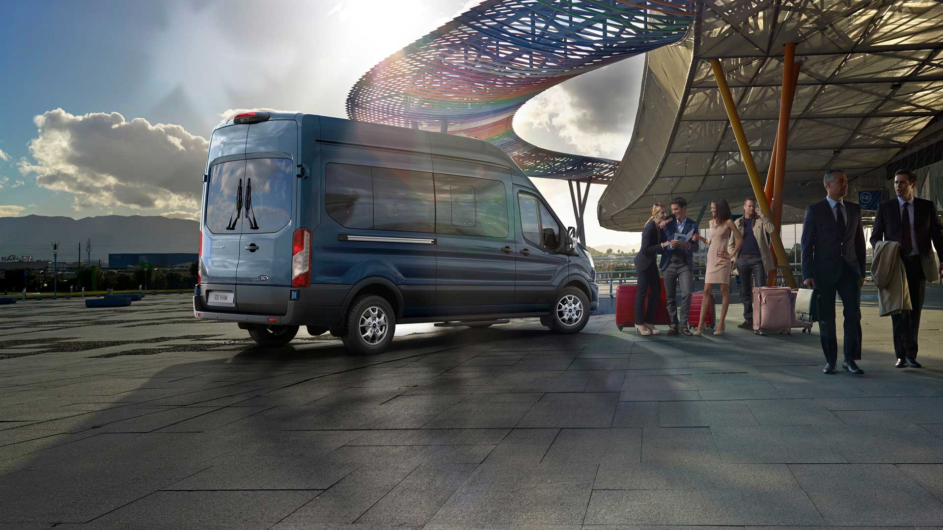 Ford Transit Bus in Blau. Heckansicht, parkt vor einem Flughafen.