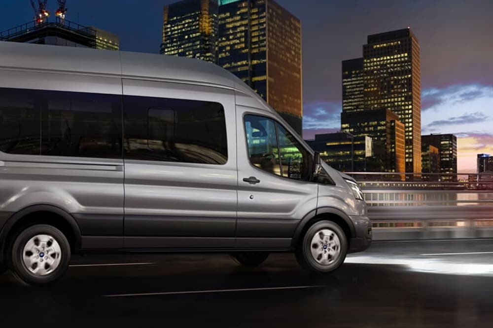 Ford Transit Bus in Silber. Dreiviertelansicht, fährt auf einer Autobahn bei Nacht.