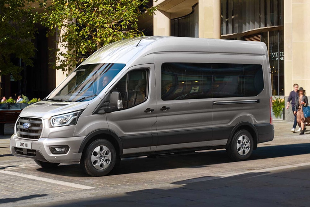 Ford Transit Bus in Silber. Seitenansicht, parkend vor einem Restaurant.