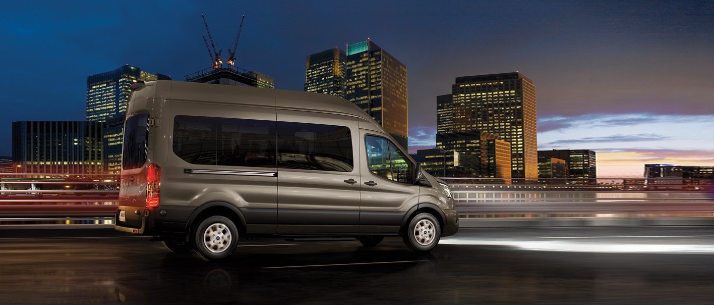 Ford Transit Bus in Silber. Dreiviertelansicht, fährt auf einer Autobahn bei Nacht