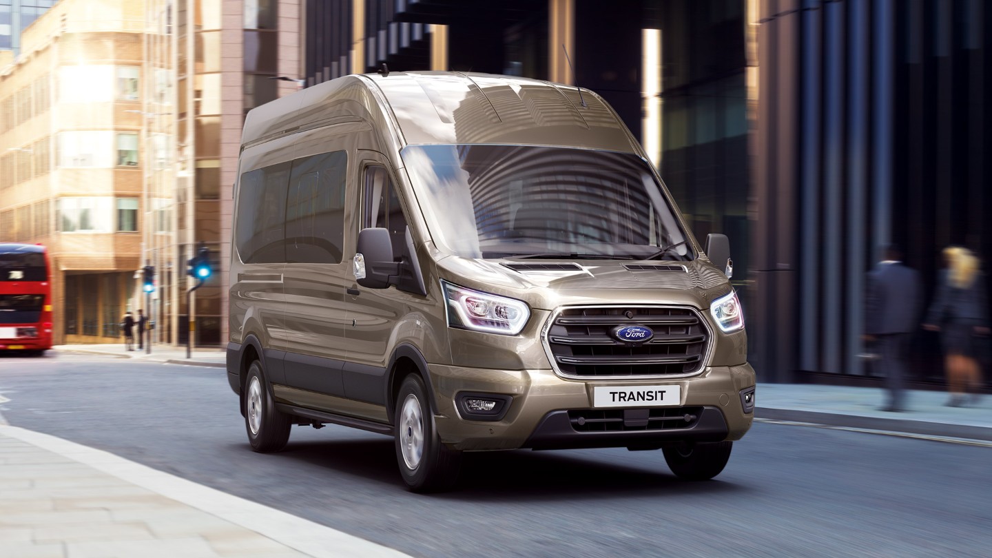 Ford Transit Bus in Silber. Dreiviertelansicht, fahrend durch die Innenstadt