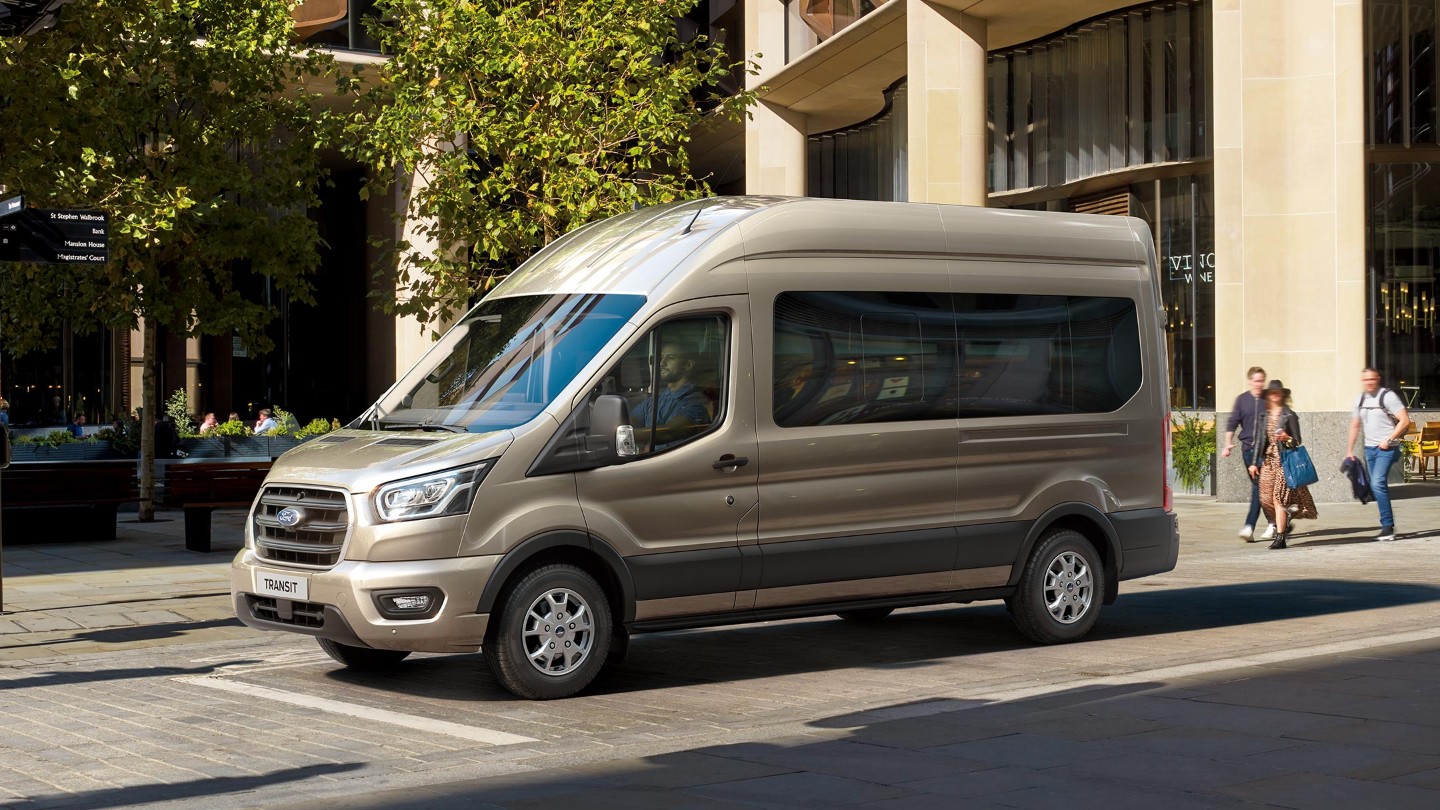 Ford Transit Bus in Silber. Seitenansicht, parkend vor einem Restaurant