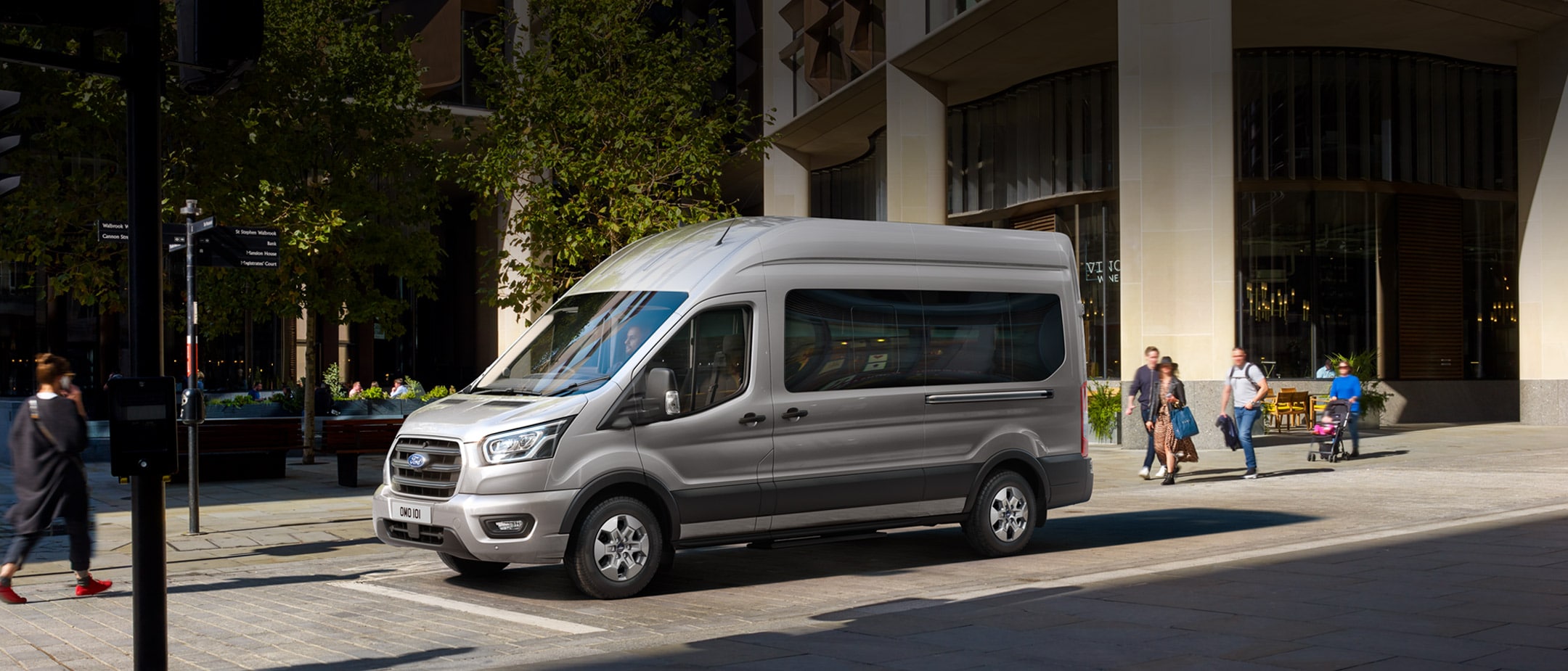 Ford Transit Bus in Silber. Seitenansicht, parkend vor einem Restaurant.