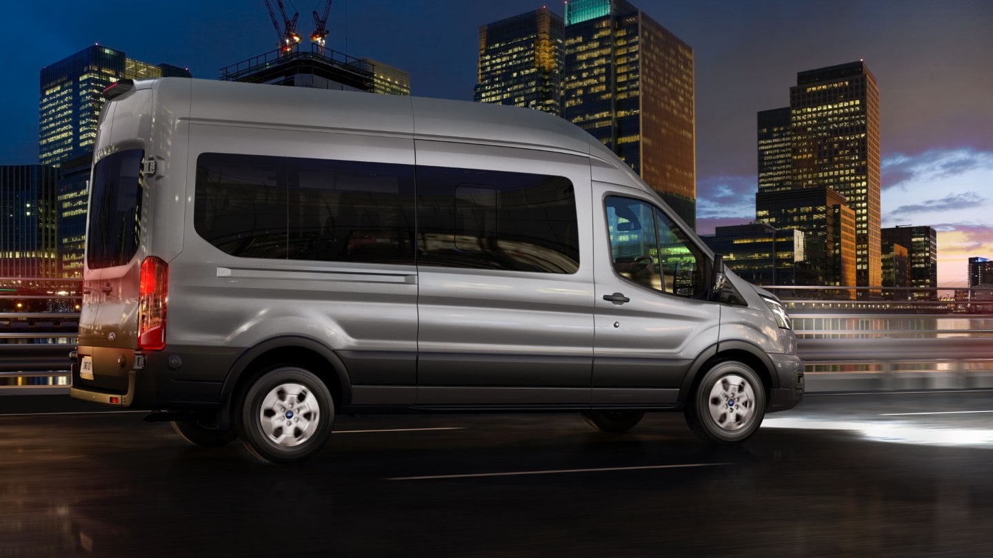 Ford Transit Bus in Silber. Dreiviertelansicht, fährt auf einer Autobahn bei Nacht.