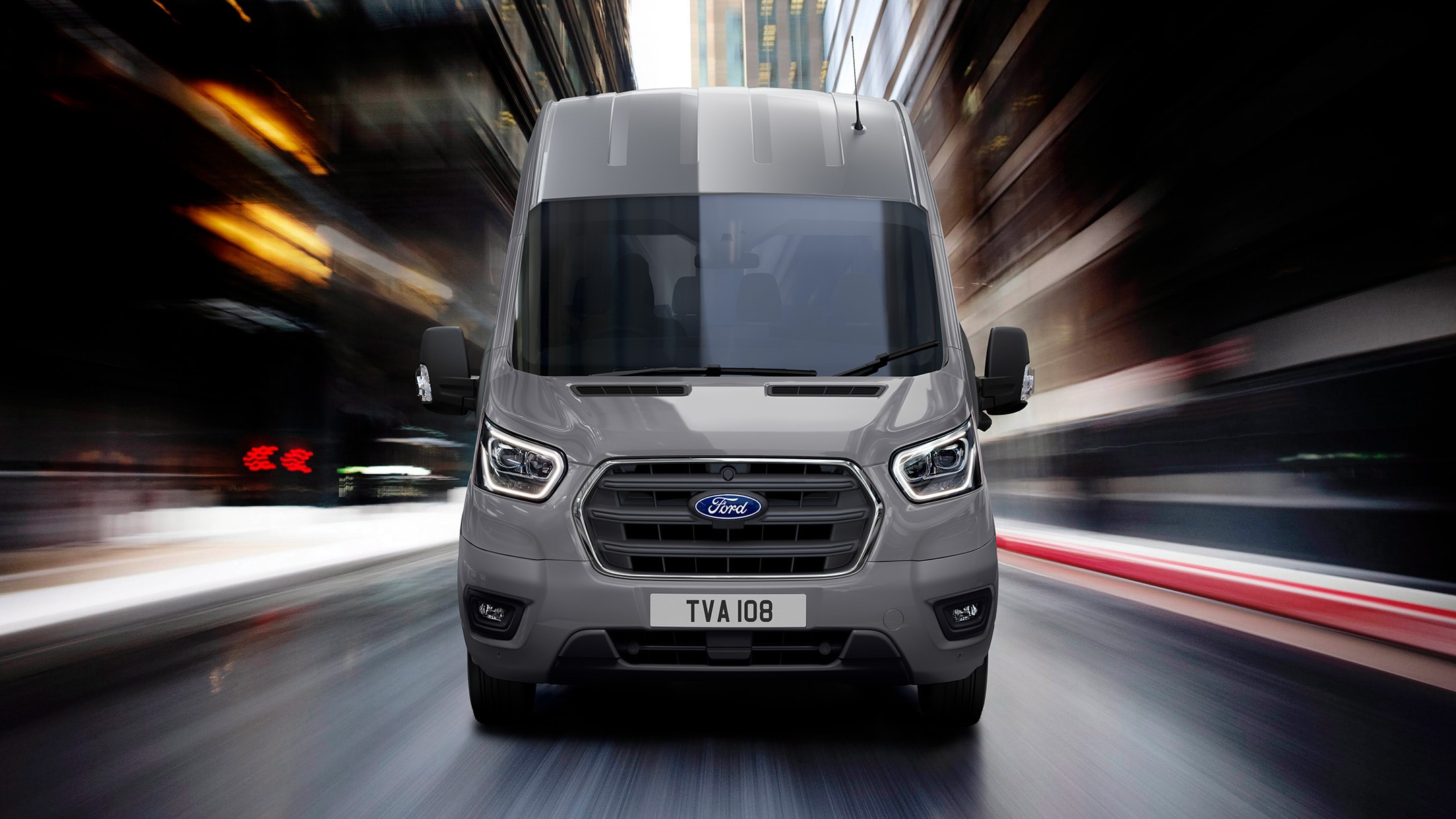 Ford Transit Bus in Silber. Frontansicht, fährt in einer Stadt.