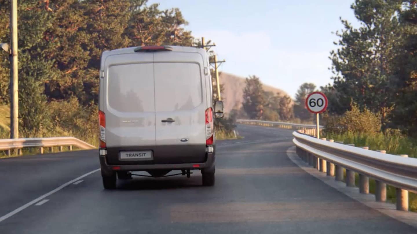 Ford Transit in Silber. Heckansicht, auf einer Landstraße fahrend