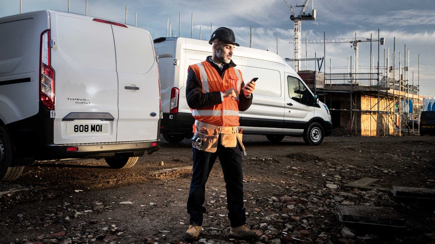 Mann auf einer Baustelle, sieht auf sein Smartphone.