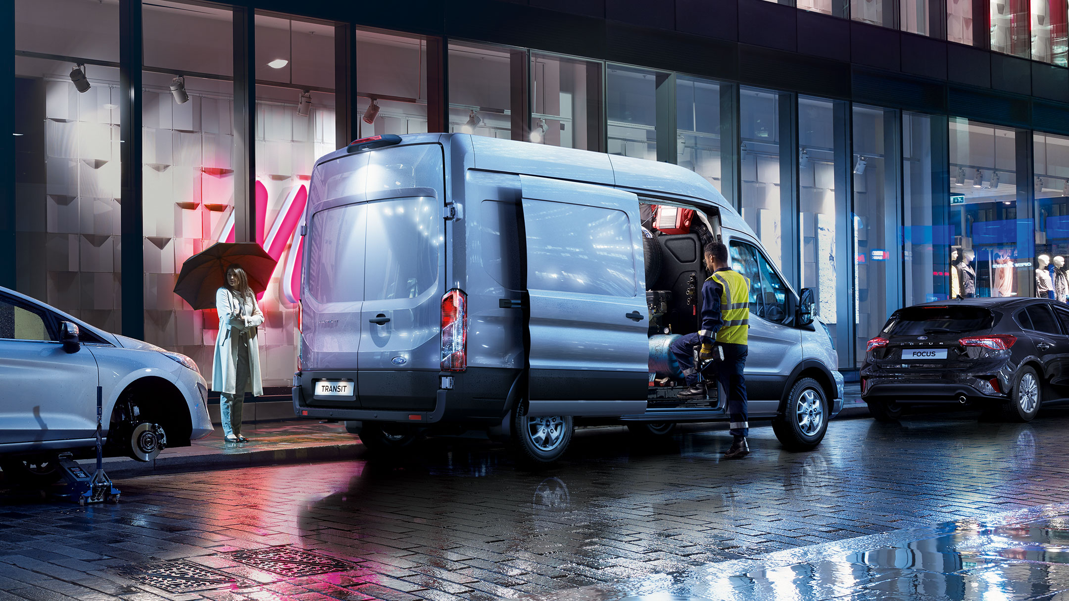 Ford Transit Kastenwagen in Blau. Seitenansicht, parkend mit geöffneter Schiebetür. Mann belädt das Fahrzeug bei Nacht