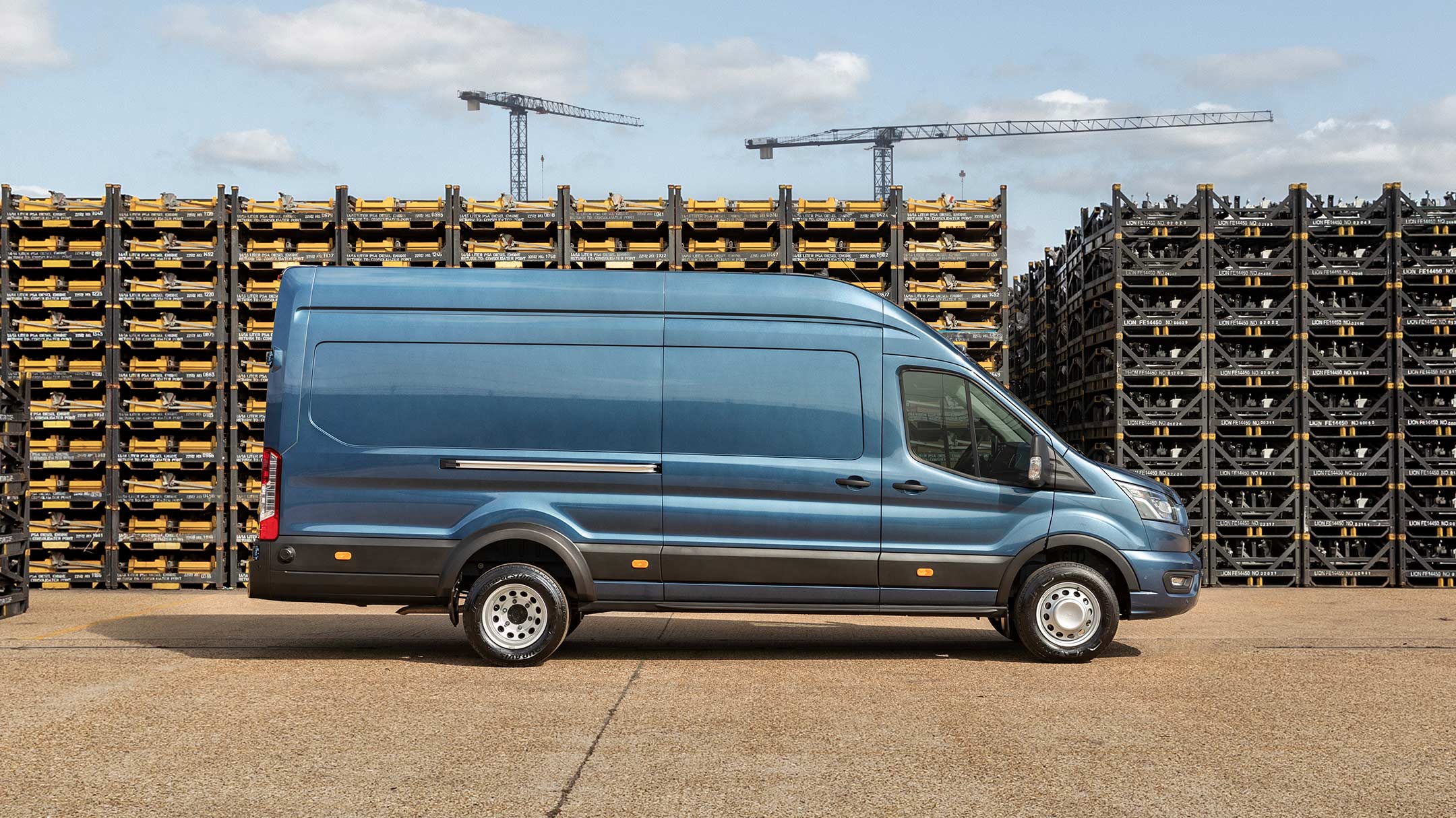 Ford Transit 5 Tonnen Kastenwagen LKW in Blau. Seitenansicht, parkend auf einem Betriebsgelände vor Palettenstapeln