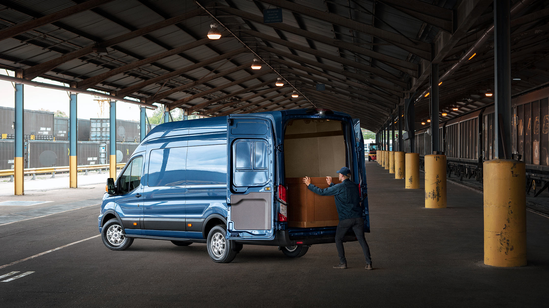 Ford Transit Kastenwagen in Blau. Dreiviertelansicht, parkend unter einem Vordach mit weit geöffneten Hecktüren