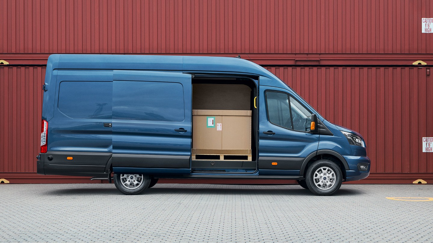 Ford Transit Kastenwagen in Blau. Seitenansicht, mit geöffneter seitlicher Schiebetüre parkt vor Frachtcontainern