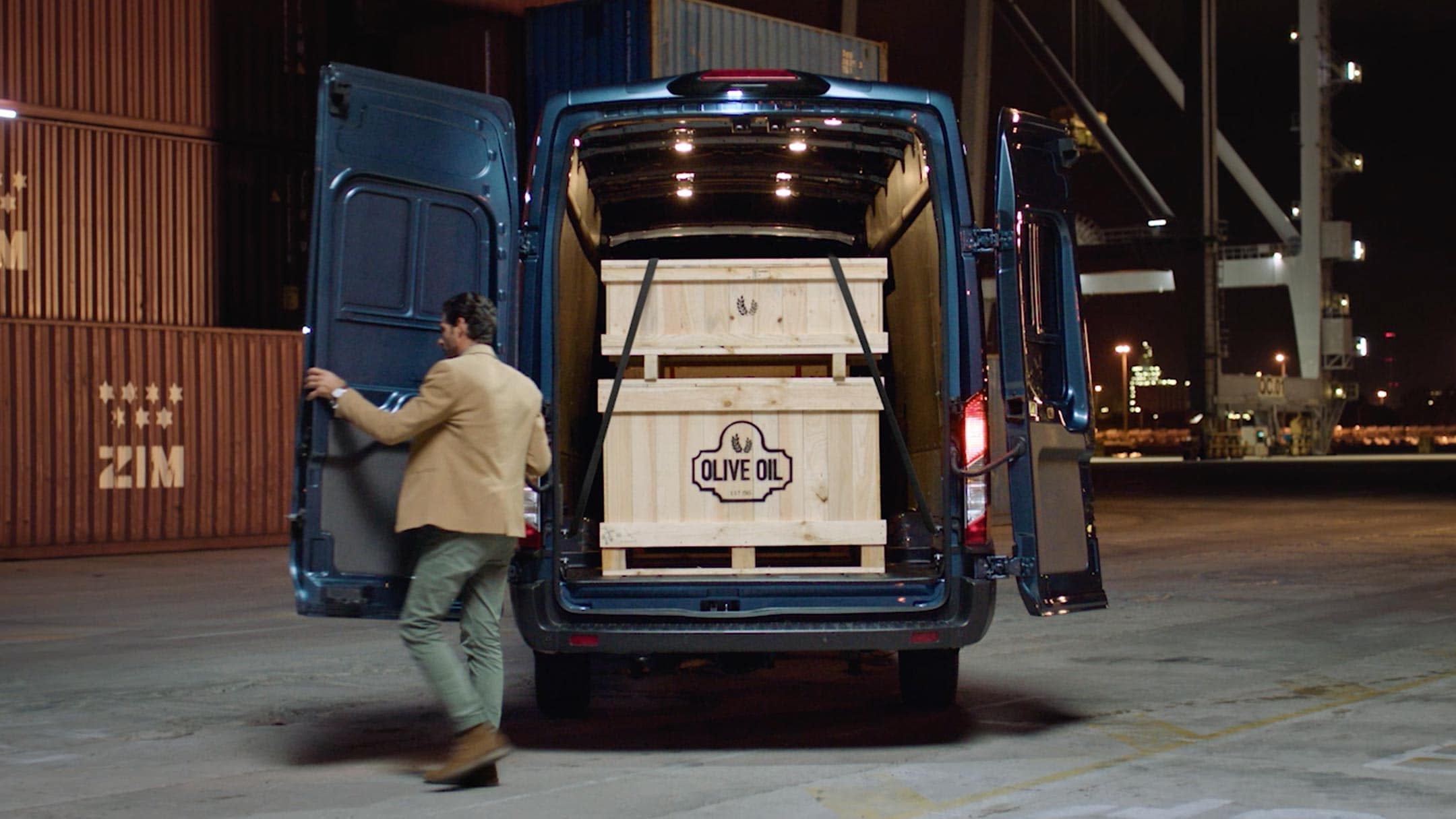 Ford Transit Kastenwagen in Blau. Heckansicht, mit geöffneten Hecktüren beladen parkt vor Frachtcontainern