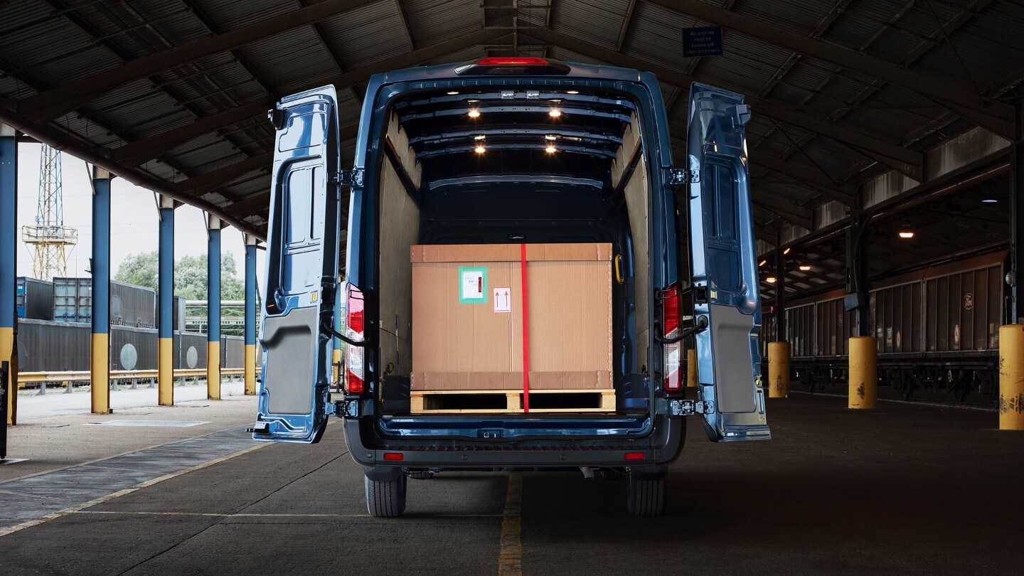 Ford Transit Kastenwagen in Blau. Heckansicht, parkend unter einem Vordach mit weit geöffneten Hecktüren und Ladung 