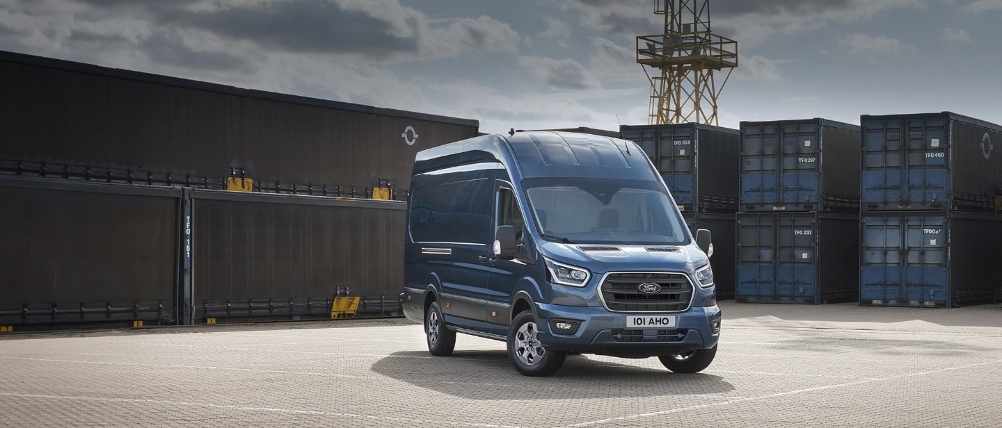 Ford Transit in Blau. Dreiviertelansicht von vorne, parkend vor Container in einem Hafen