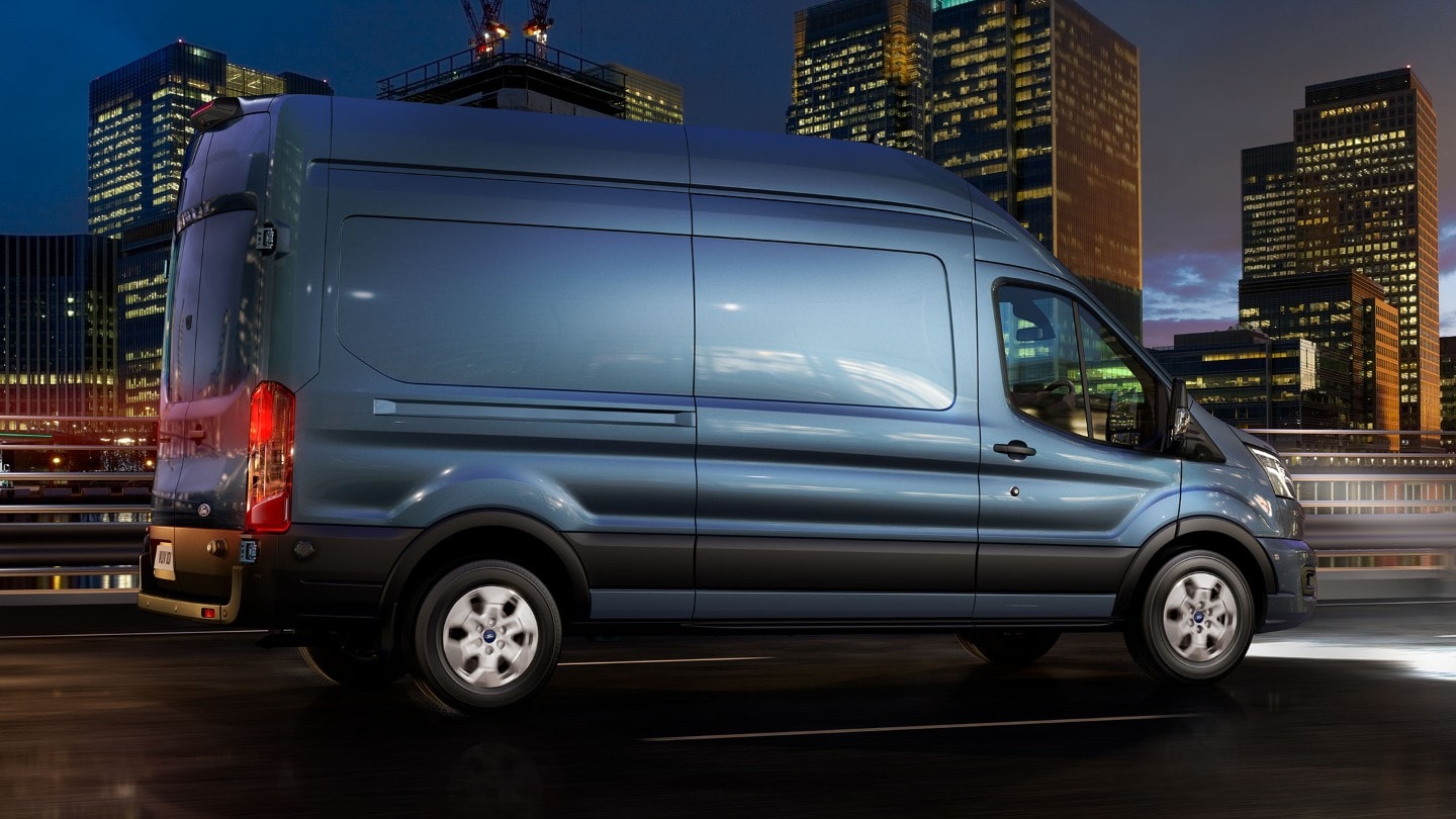 Ford Transit in Blau. Seitenansicht, fahrend auf einer Straße bei Nacht mit Auto-Hochbeleuchtung.