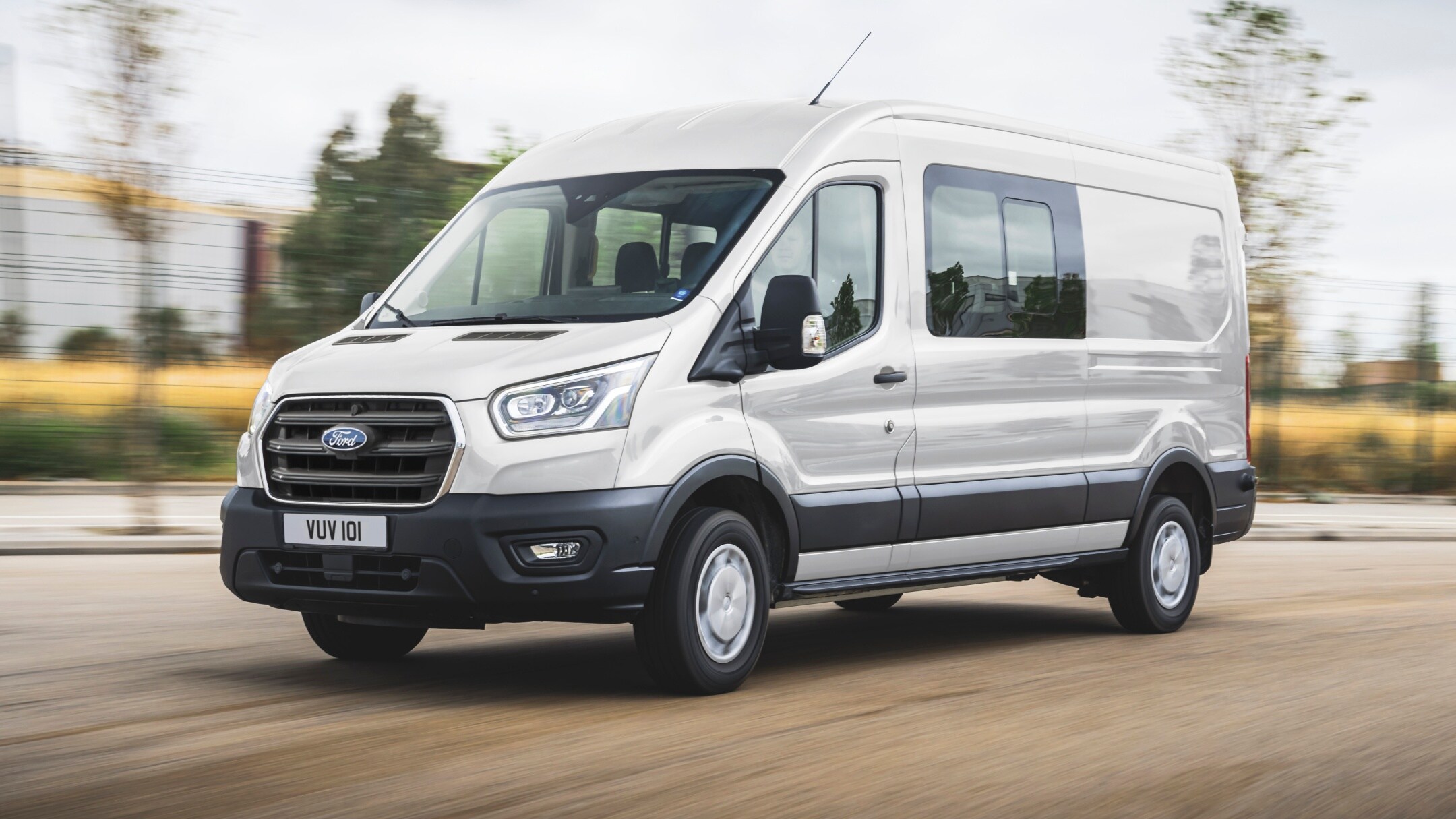 Ford Transit in Weiß. Dreiviertelansicht, fahrend auf einer Straße.