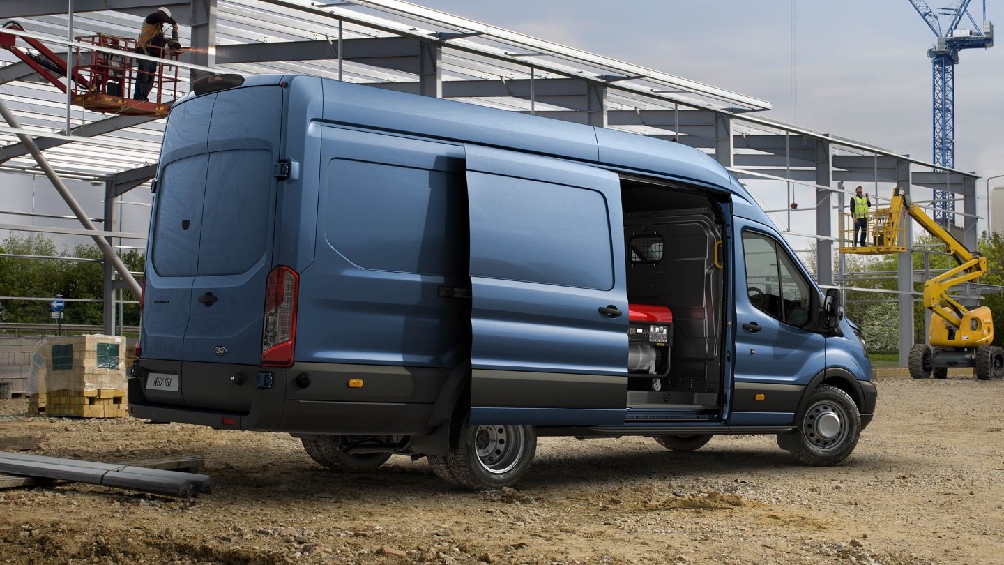 Ford Transit in Blau. Seitenansicht, stehend vor Baumstelle mit geöffneter Seitentür.