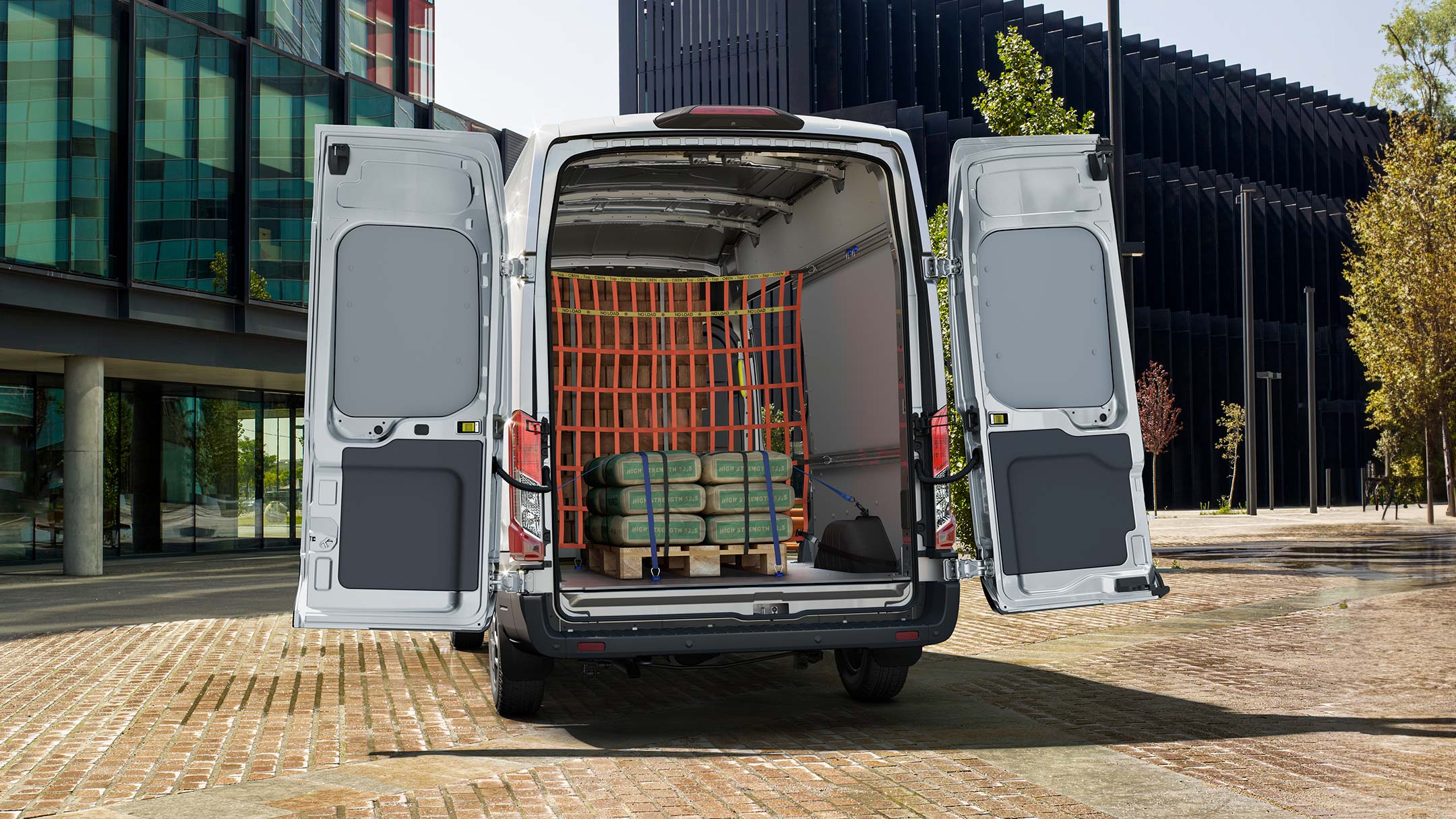 Ford Transit in Weiß. Heckansicht, parkend vor einem Gebäude mit geöffneter Hecktür.