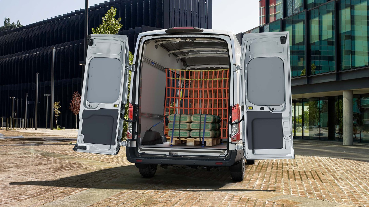 Ford Transit in Weiß. Heckansicht, parkend vor einem Gebäude mit geöffneter Hecktür.