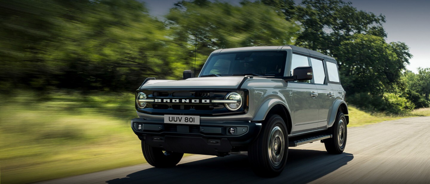 Ford Bronco in Rot. Frontansicht, fahrend in den Bergen durch einen Fluss.