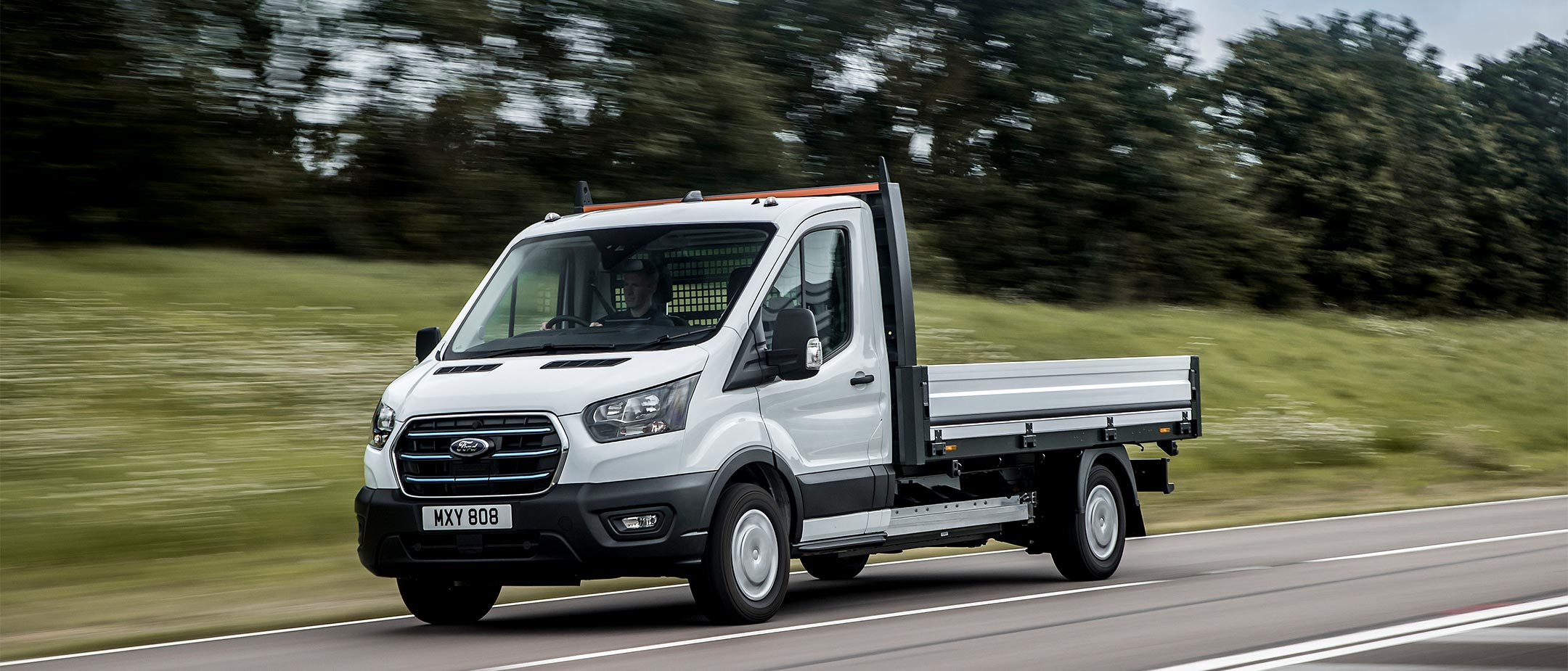 Ford E-Transit Fahrgestell in Weiß. Dreiviertelansicht, fahrend auf einer Straße. 