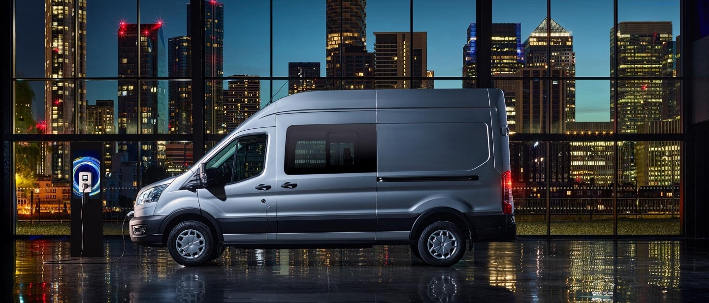 Ford E-Transit Doppelkabine in Blau. Seitenansicht, an einer Ladestation angeschlossen.