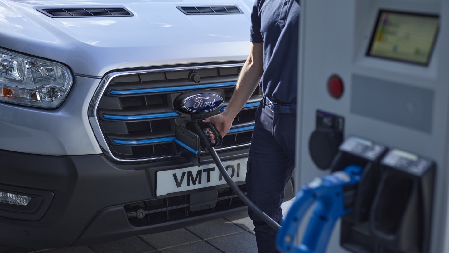 Ford E-Transit in Silber. Detailansicht des Ladeanschluss mit Ladekabel und Ladesäule.