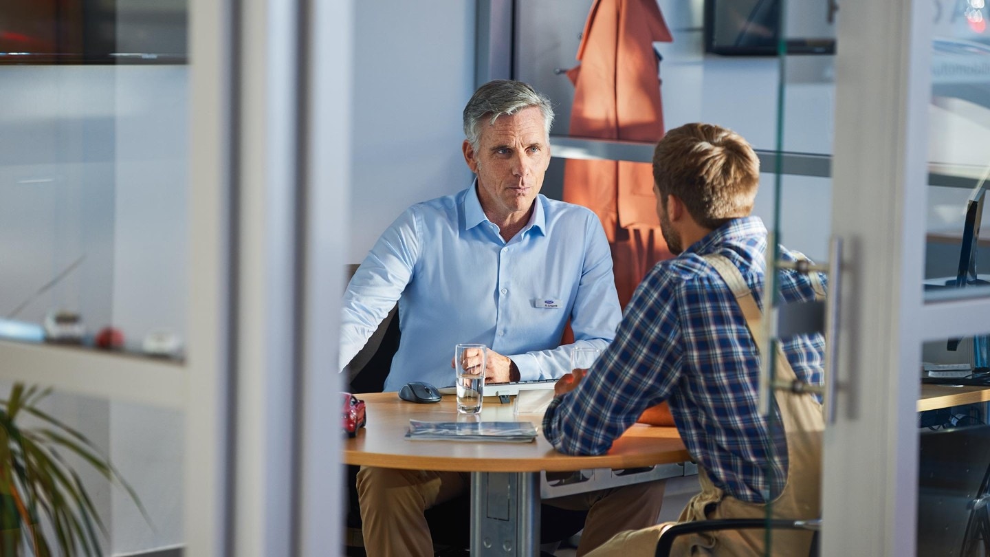 Zwei Männer sitzen an einem Büroschreibtisch gegenüber voneinander 