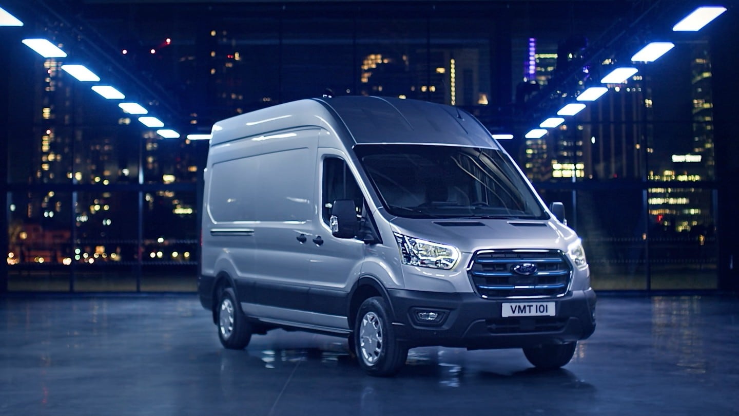 Ford E-Transit in Silber. Dreiviertelansicht, stehend in einer Lagerhalle.