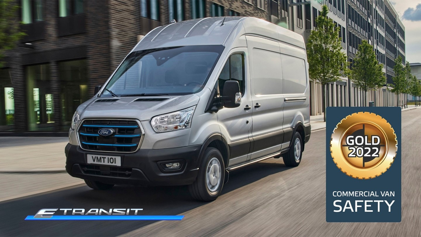 Ford E-Transit Kastenwagen in Silber. Dreiviertelansicht, fährt entlang Hochhäusern und NCAP Gold-Logo für Kategorie „Sicherheit“