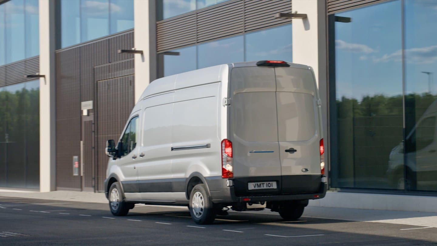 Ford E-Transit in Silber. Heckansicht, parkt vor modernem Gebäude