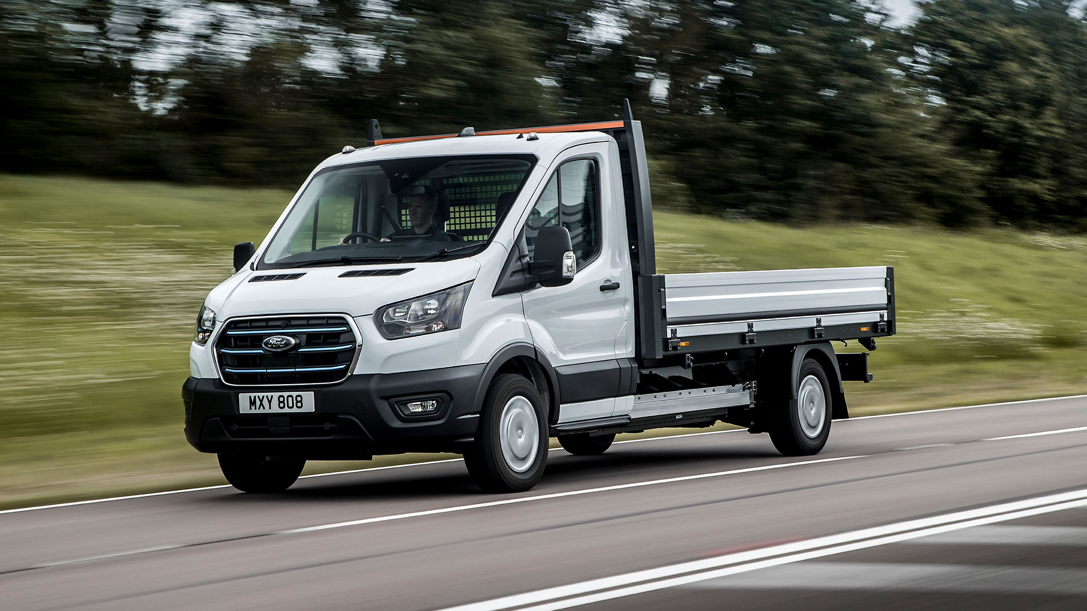 Ford E-Transit Fahrgestell in Weiß. Dreiviertelansicht, auf einer Landstraße fahrend