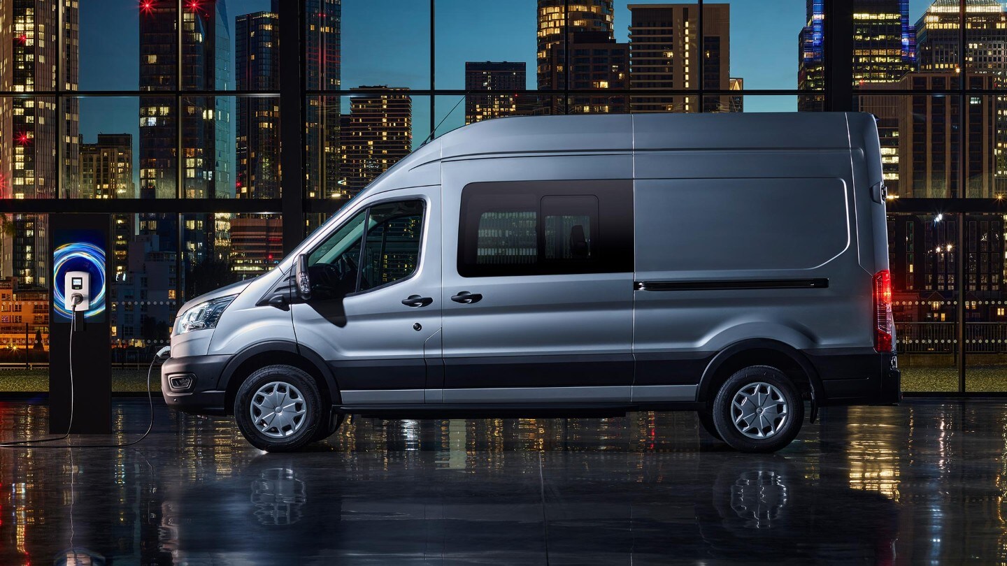 Ford E-Transit Doppelkabine in Blau. Seitenansicht, an einer Ladestation angeschlossen.