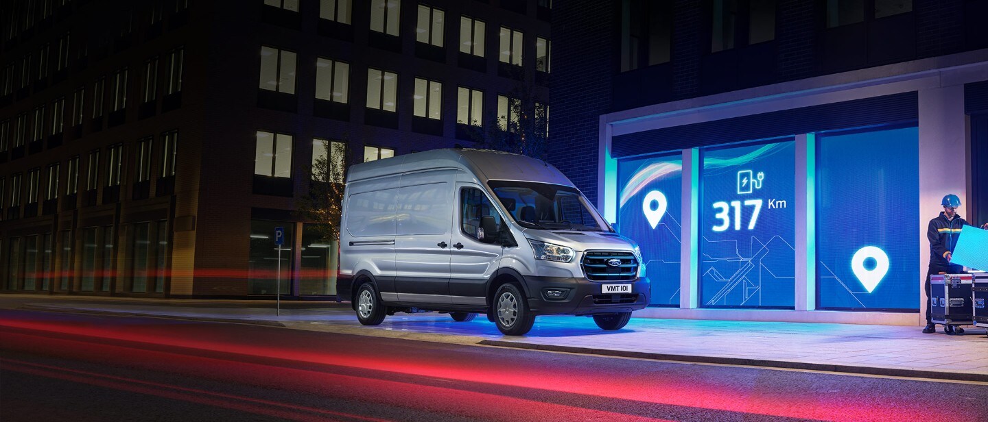 Ford E-Transit in Silber. Dreiviertelansicht, in einer Stadt bei Nacht