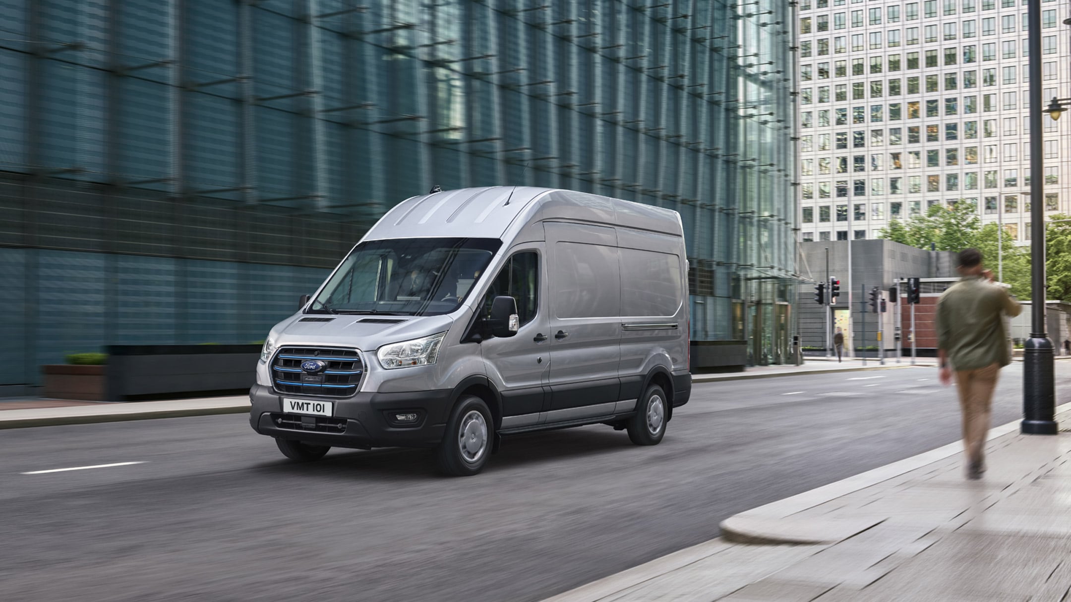 Ford E-Transit Kastenwagen in Silber. Dreiviertelansicht, fahrend durch die Stadt