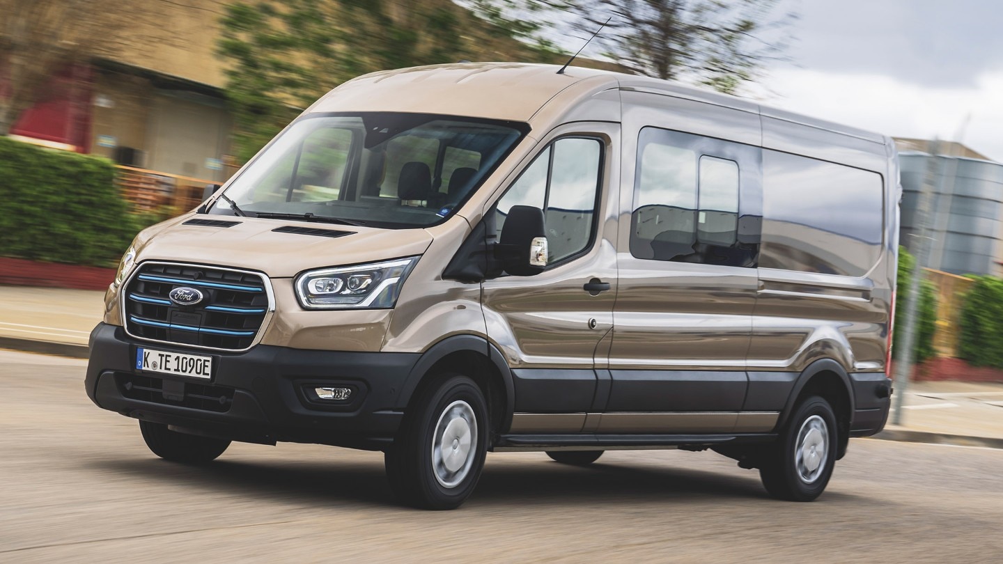 Ford E-Transit Doppelkabine in Silber. Dreiviertelansicht, fahrend auf einer Straße.