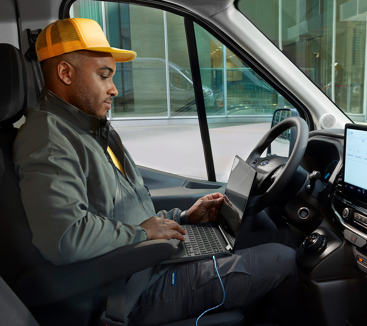 Mann sitzt im Ford E-Transit auf dem Fahrersitz, mit einem angeschlossenen Laptop.