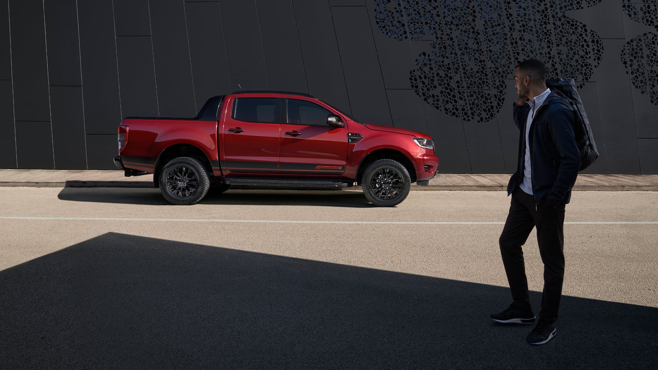 Ford Ranger Stormtrak in Rot. Seitenansicht, parkend am Straßenrand und Mann im Vordergrund