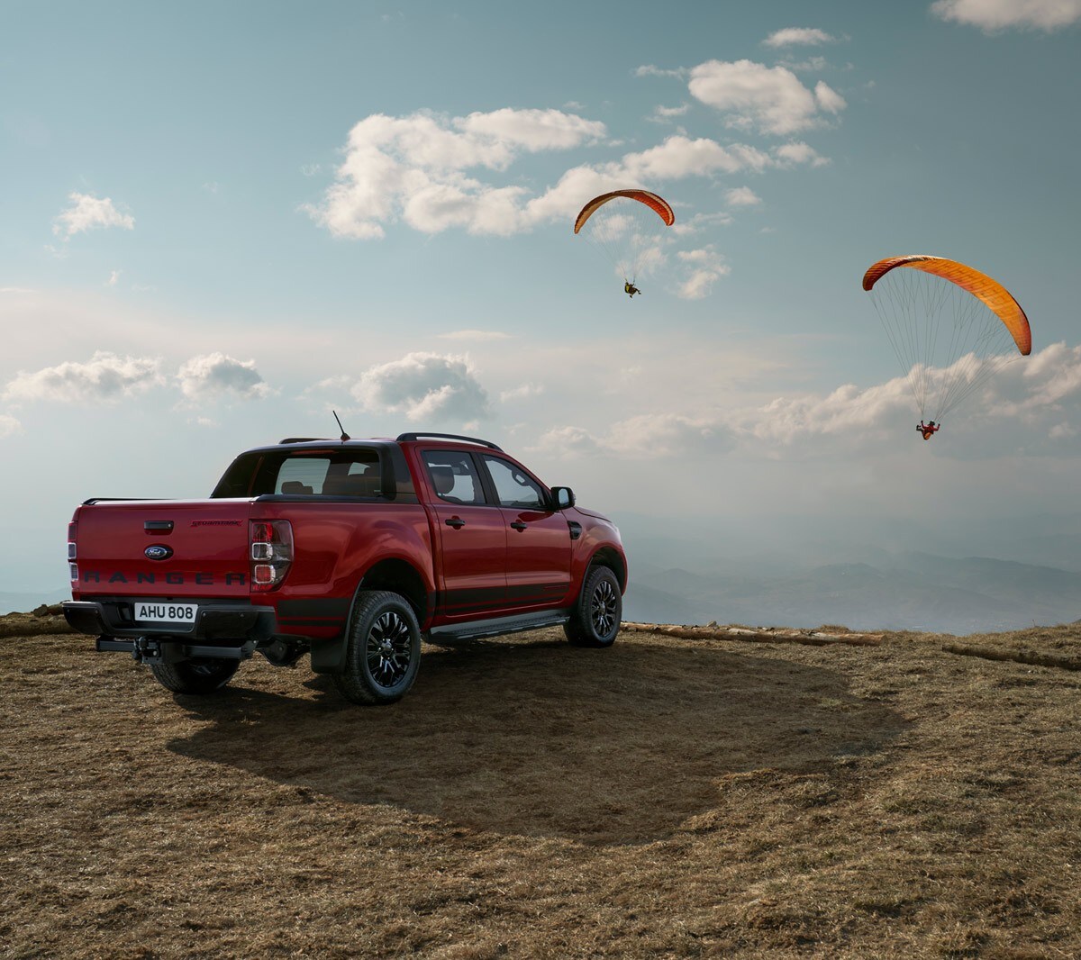 Ford Ranger Stormtrak in Rot. Dreiviertelansicht, parkend in Dünenlandschaft und Paraglider am Himmel