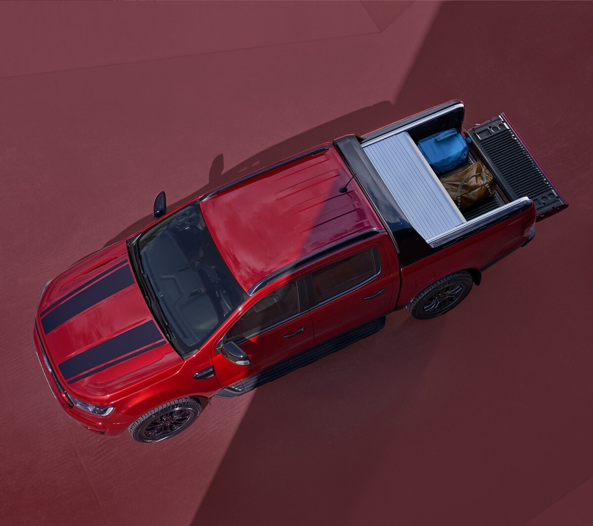 Ford Ranger Stormtrak in Rot. Vogelperspektive mit geöffnetem Laderaumrollo, parkend auf rotem Untergrund 