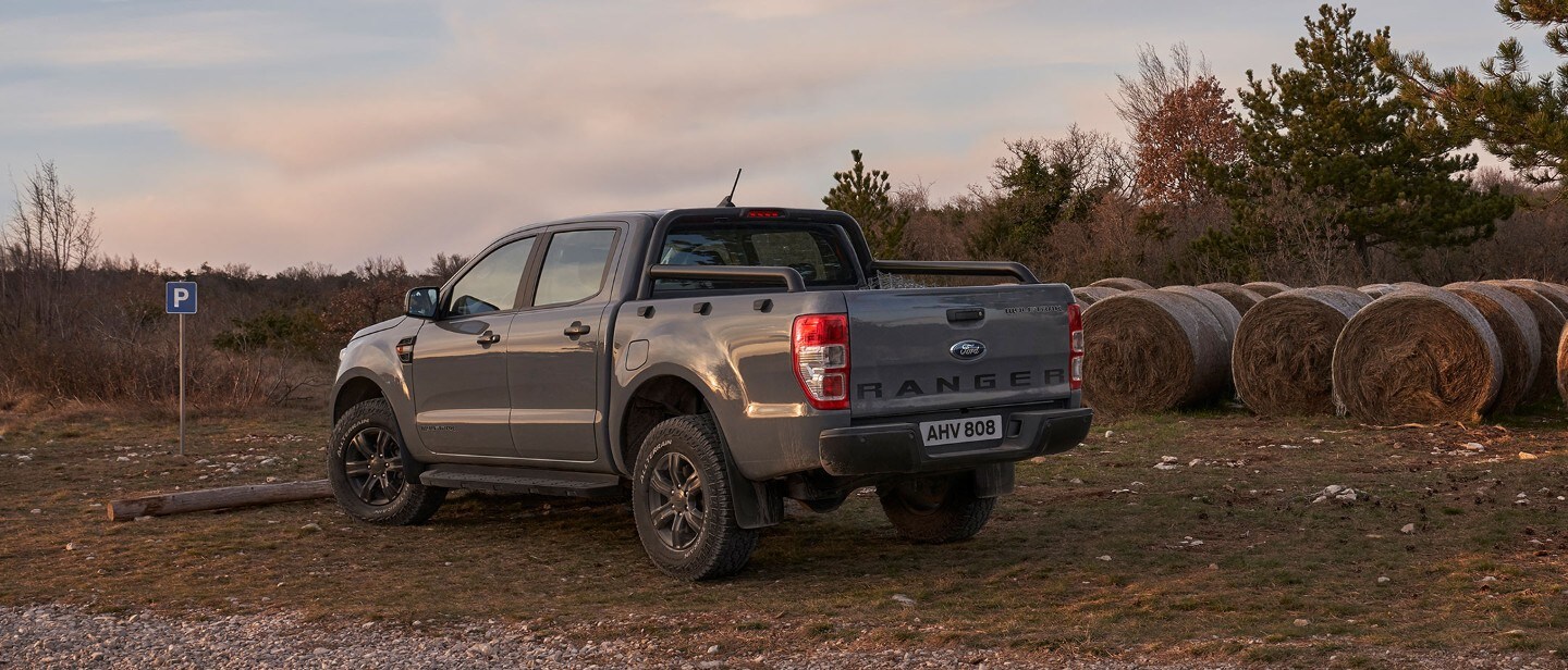 Ford Ranger Wolftrak in Grau. Dreiviertelansicht von hinten, parkend auf einer Landwirtschaftsfläche neben Heuballen