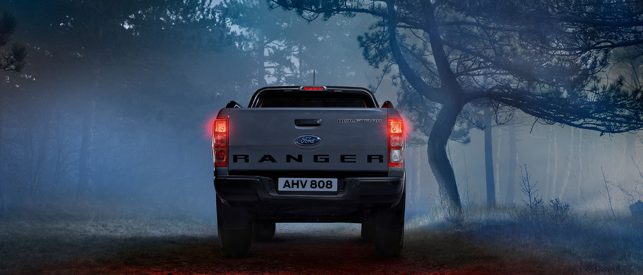 Ford Ranger Wolftrak in Grau. Heckansicht, parkend auf einem Waldweg bei Dämmerung und Nebel
