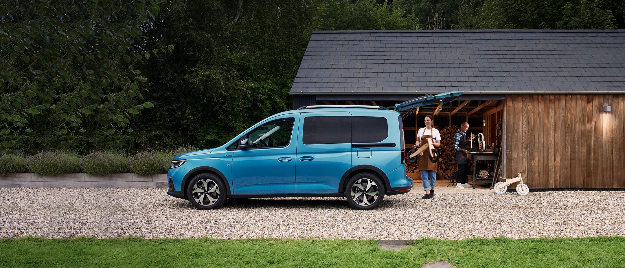 Ford Tourneo Connect in Blau. Seitenansicht, vor einer Holzhütte