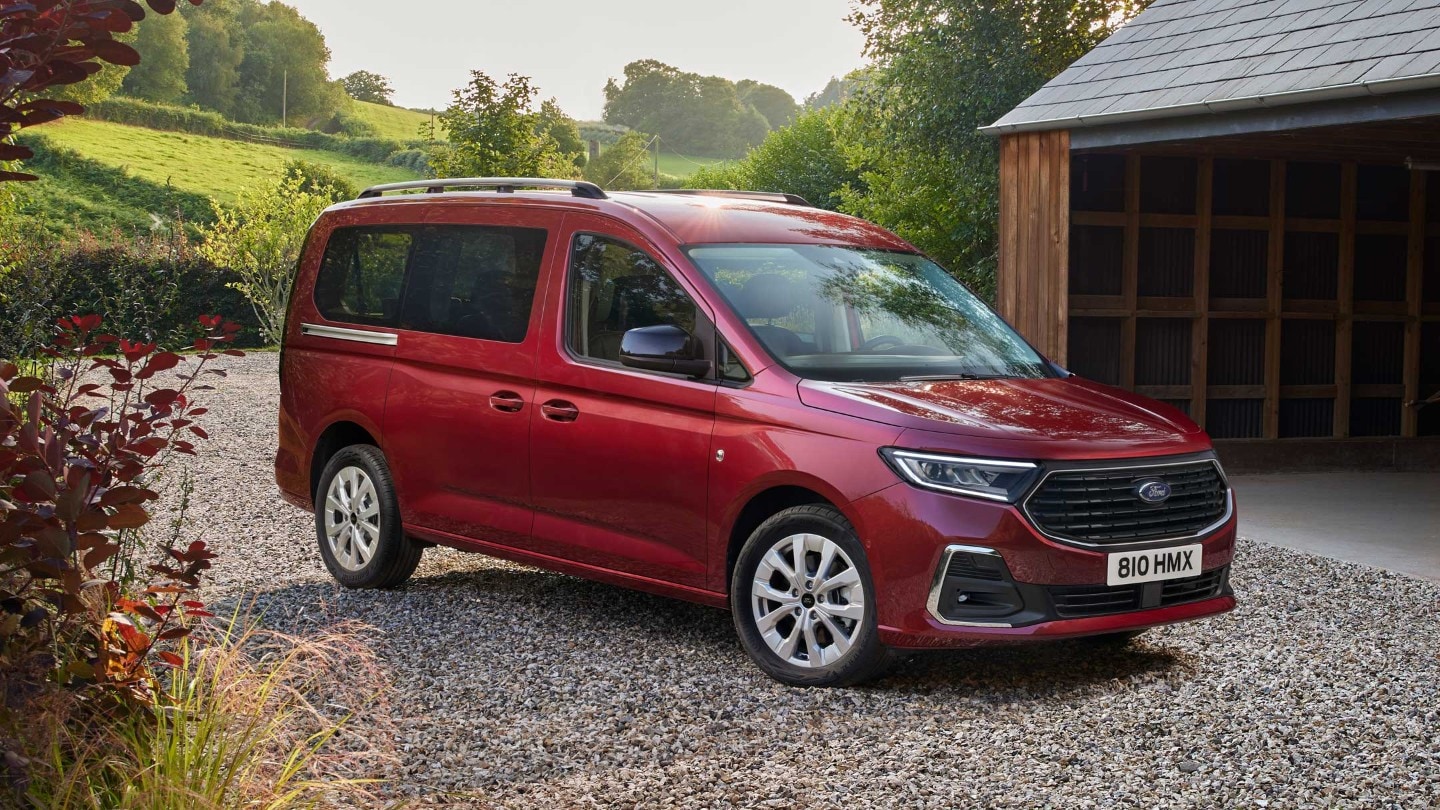 Ford Grand Tourneo Connect in Rot. Dreiviertelansicht, parkt auf Kiesweg vor Wohnhaus 