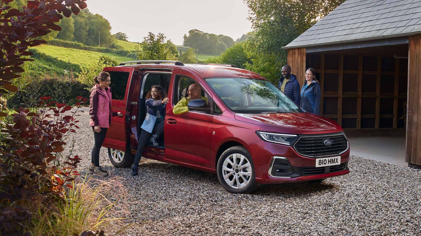 Ford Grand Tourneo Connect in Rot. Dreiviertelansicht, parkt auf Kiesweg vor Wohnhaus 