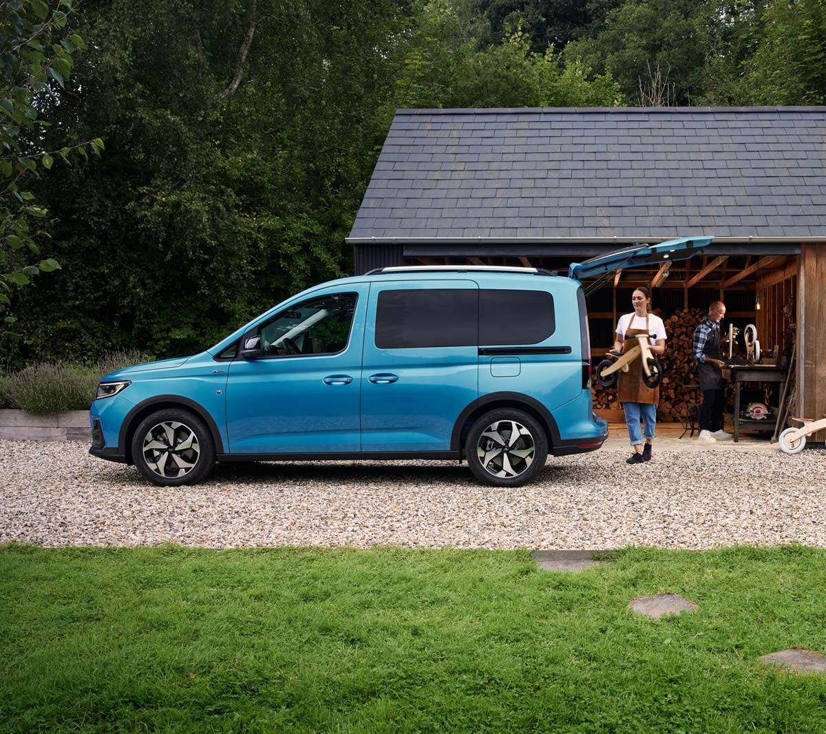 Ford Tourneo Connect in Boundless Blue. Seitenansicht, mit geöffneter Hecktür, Frau belädt Gepäckraum