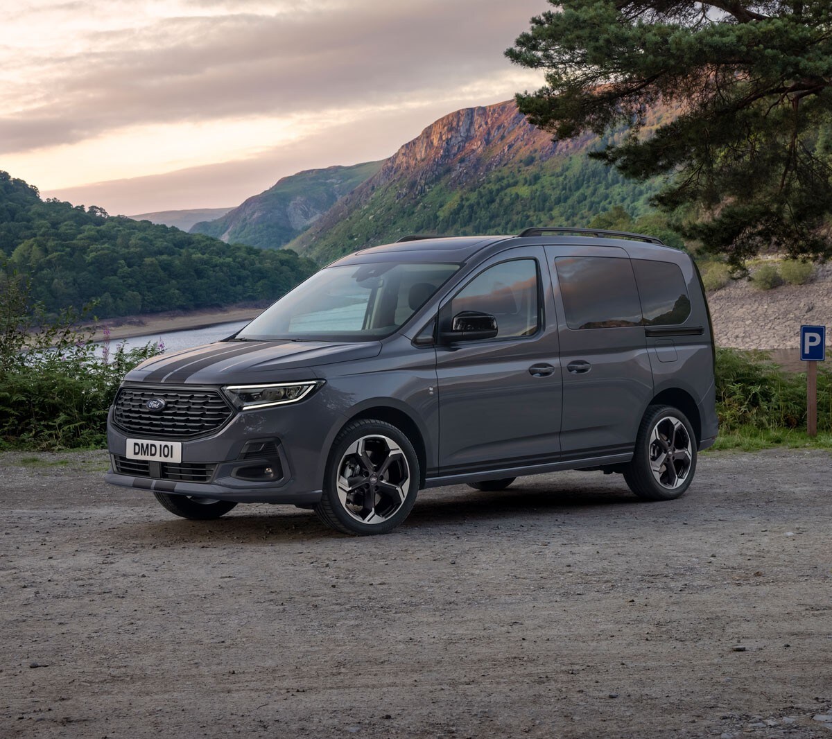 Ford Tourneo Connect in Grau. Dreiviertelansicht, parkt vor gebirgiger Landschaft mit Fluss im Hintergrund